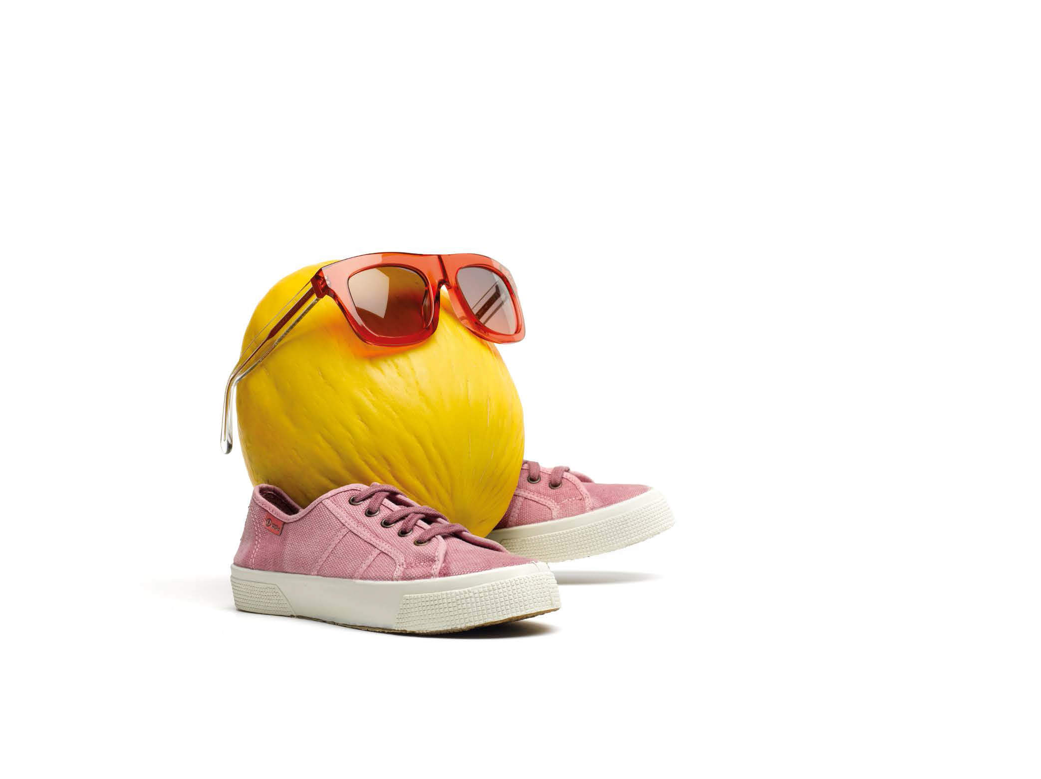 Eine gelbe Melone mit roter Sonnenbrille und rosa Turnschuhen sitzt auf einem weißen Hintergrund, was ihr ein verspieltes und schrulliges Aussehen verleiht.