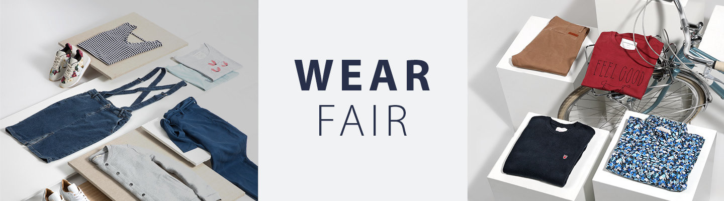 Es werden Kleidungsstücke wie ein gestreiftes Hemd, Jeans, ein Pullover und Turnschuhe ausgestellt. In der Mitte steht „Wear Fair“. Auf der rechten Seite ist neben gefalteter Kleidung ein Fahrrad teilweise zu sehen.