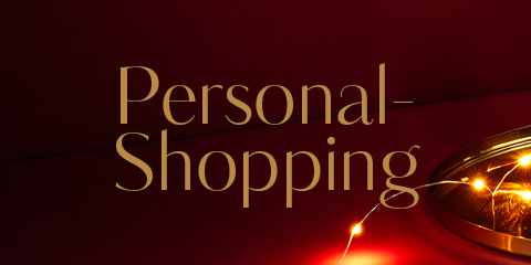 Das Bild zeigt den Schriftzug „Personal-Shopping“ in eleganter Goldschrift auf dunkelrotem Hintergrund mit dezenten Dekolichtern.