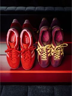 Zwei Paar Adidas-Sneaker auf einer Bank: ein rotes Paar mit weißen Streifen, das andere in Bordeauxrot und Lila mit gelben Streifen und Schnürsenkeln.